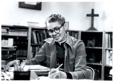 Pauli Murray, smiling while sitting at a desk, writing