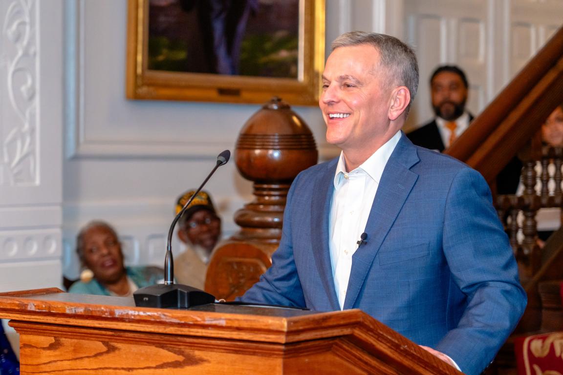 Governor Josh Stein standing at a podium, smiling