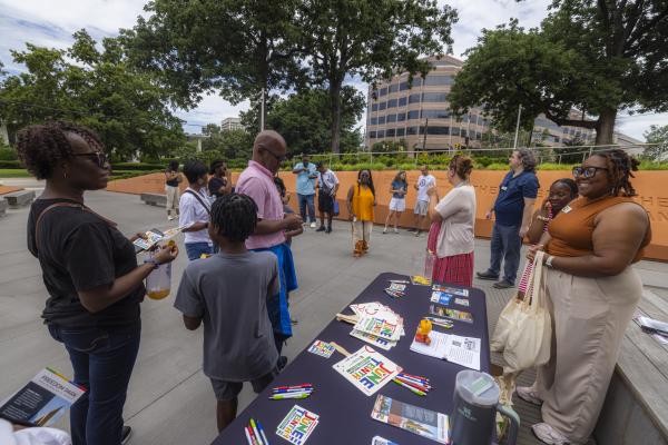 A crowd of people in Freedom Park, smiling and talking, a table with Juneteenth materials in the center.