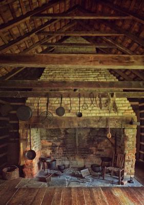 Wooden and brick interior with a brick fireplace with kitchen appliances hanging over it and appliances across the floor with a chair and basket next to them.