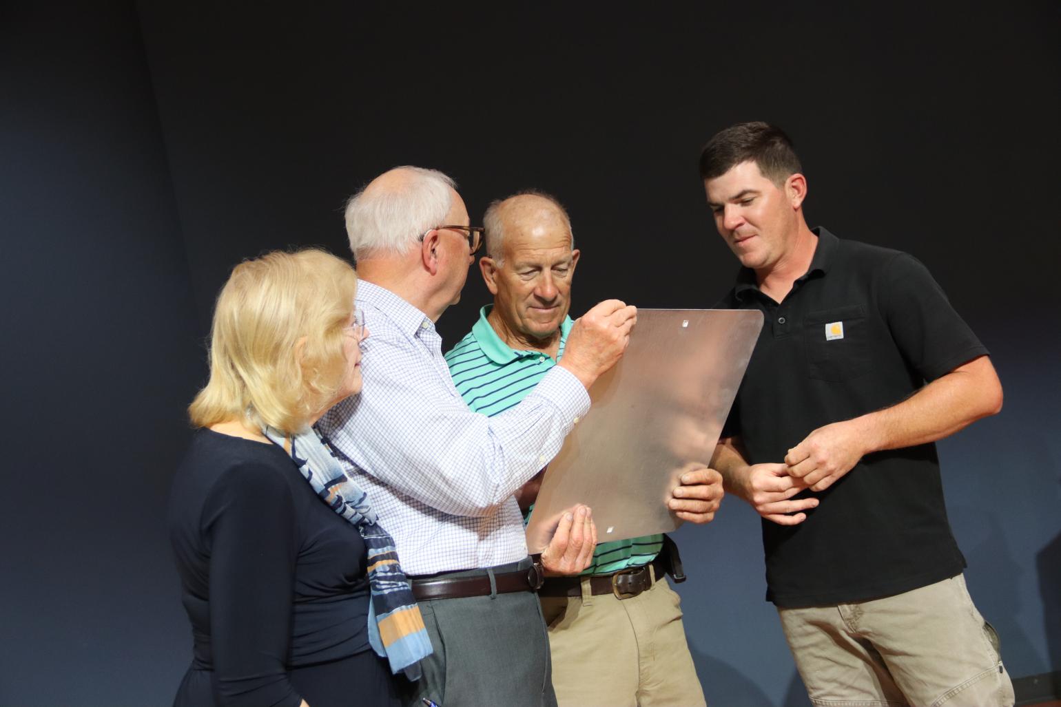 Four people look at a metal sign. 