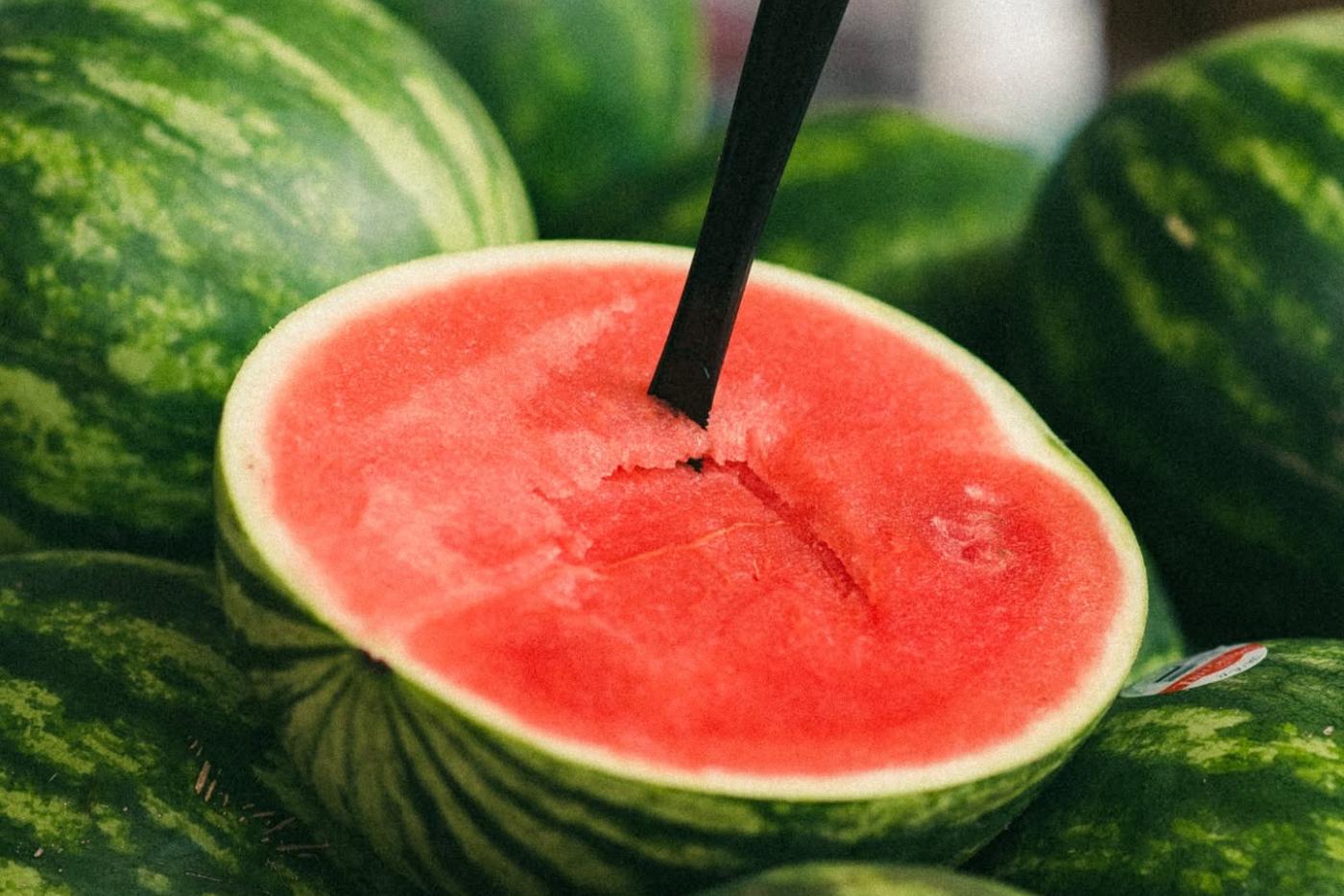 grouping of watermelons with one cut in half showing the inside of the fruit