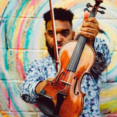 Man holding violin in front of colorful wall 
