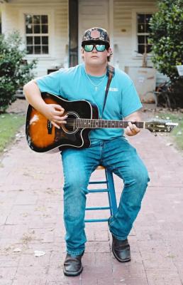 Guy playing guitar sitting on a stool 