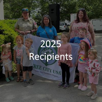 An NCFS ranger in uniform and holding a Tree City USA banner with a group of citizens during a recognition event