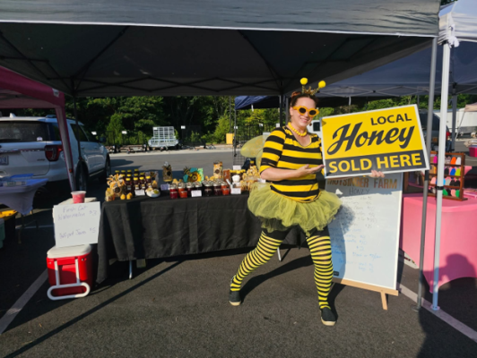 A woman in a bee costume stands outside a booth selling honey.