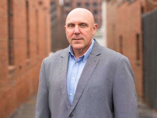 Man in grey sports coat and blue button-down shirt identified as Tim Baumgartner