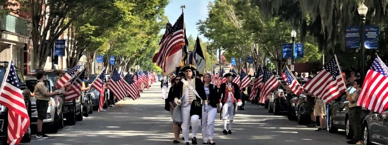 Historical interpreters dressed as soldiers, holding American flag in a parade.