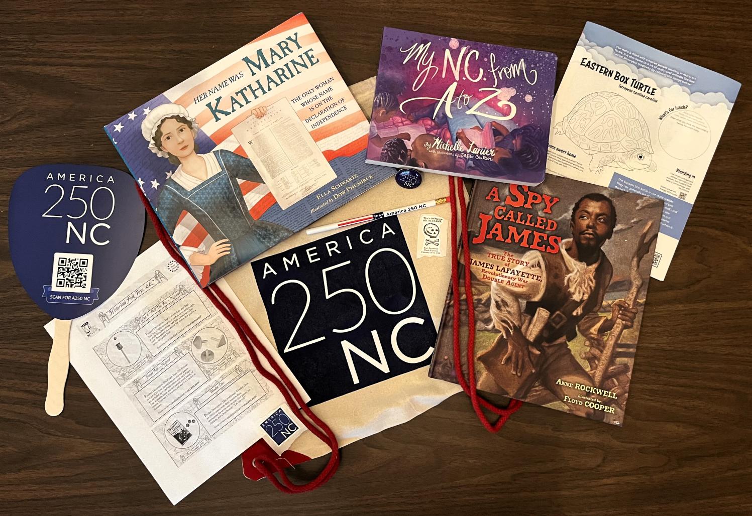 Children's books and America 250 NC branded gear spread on a table