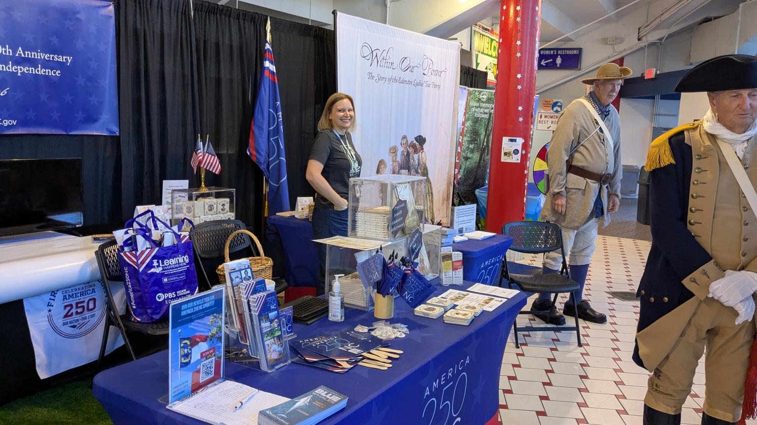 Women smiles at the camera in front of an America 250 NC table