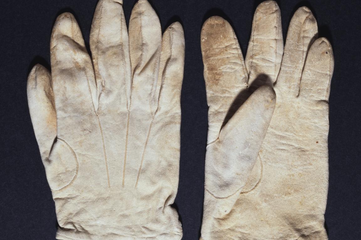 Two white deerskin gloves, one facing upwards and one facing downward, on a black background.