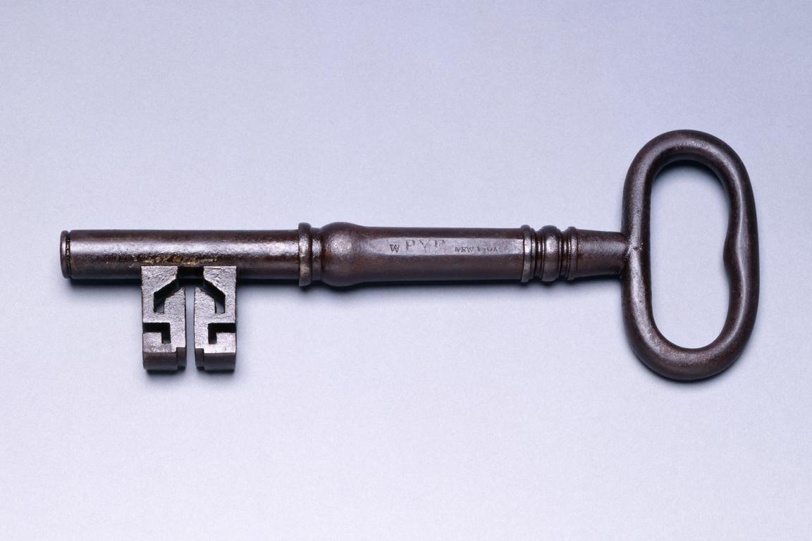 An antique metal key laying horizontally on against light background.