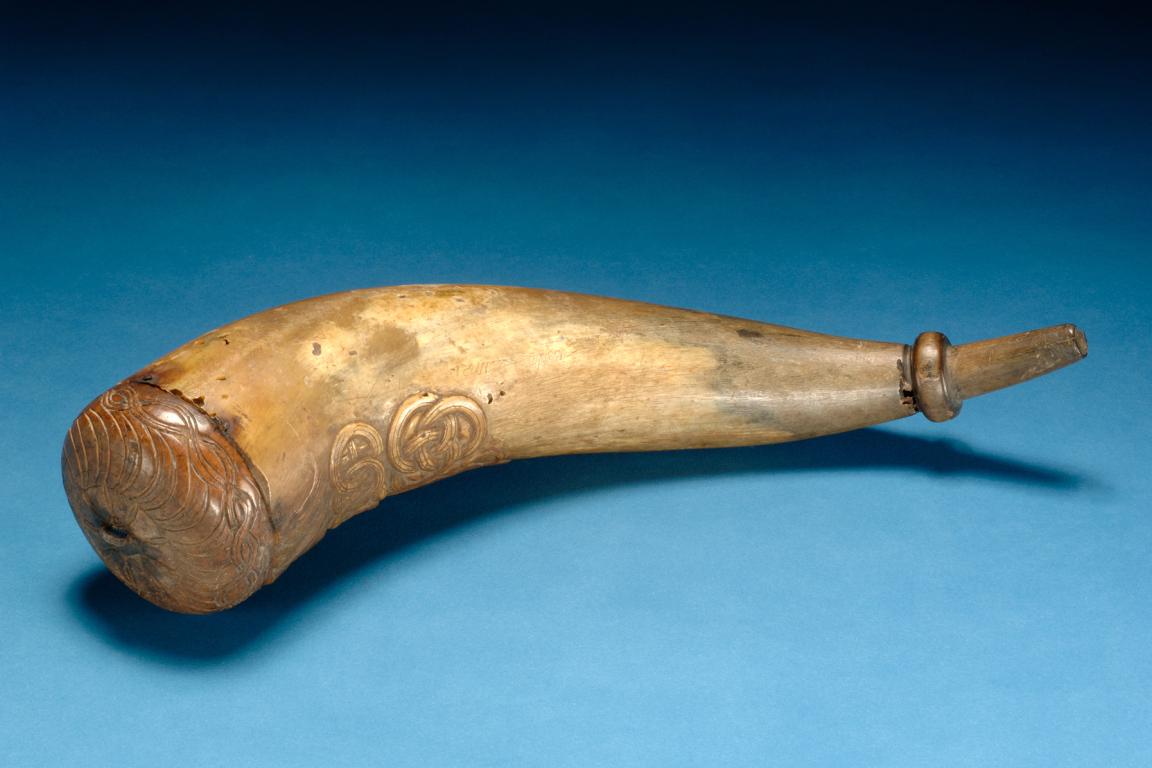 A tan horn with carved decorative patterns and a capped end over a blue background.