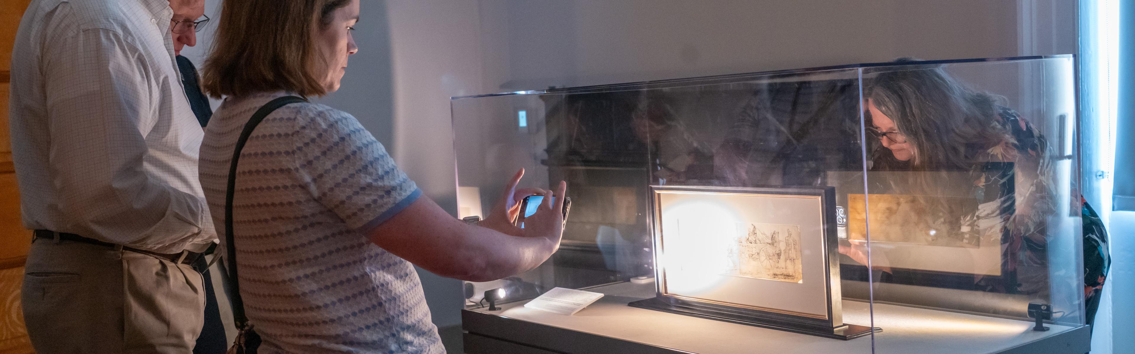 Two people take images of a sketch in a glass case