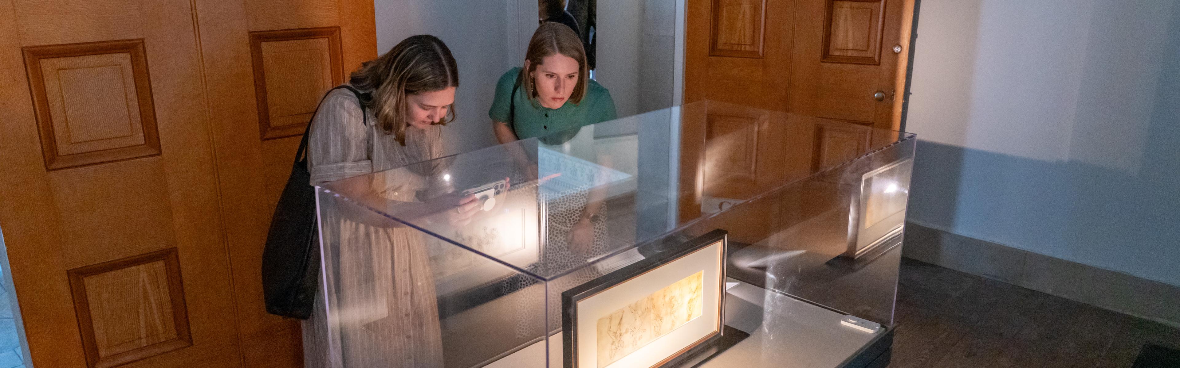 Women view a sketch in a glass case