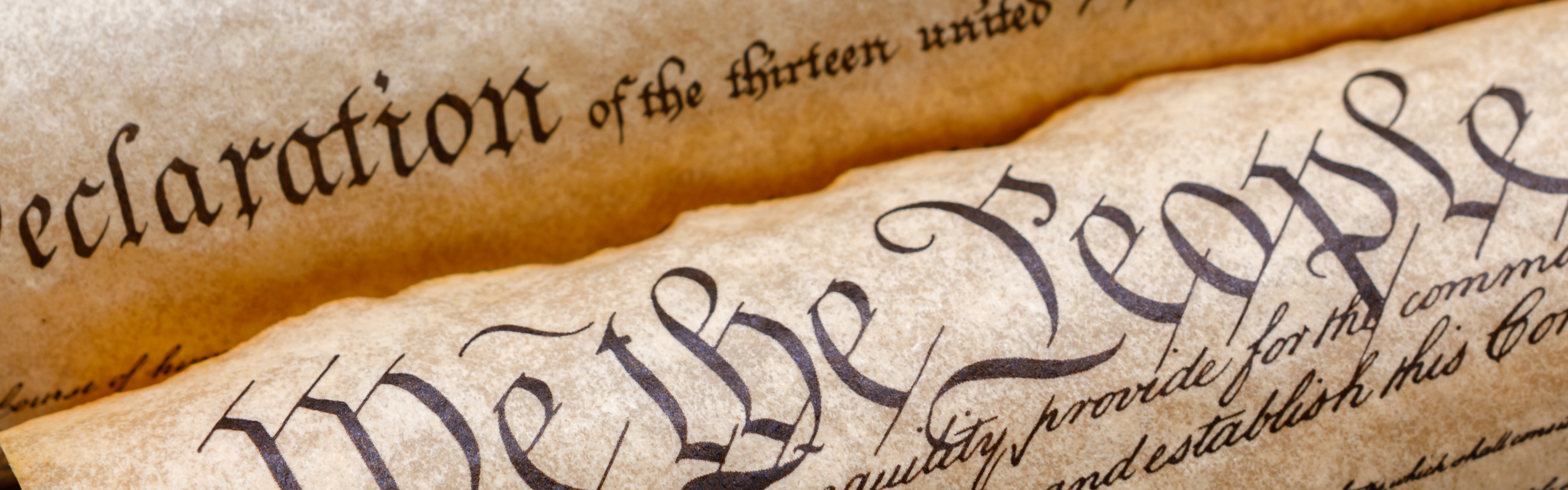 Close-up of aged parchment copies of the United States Constitution and Declaration of Independence, with prominent historic calligraphy and rolled edges.