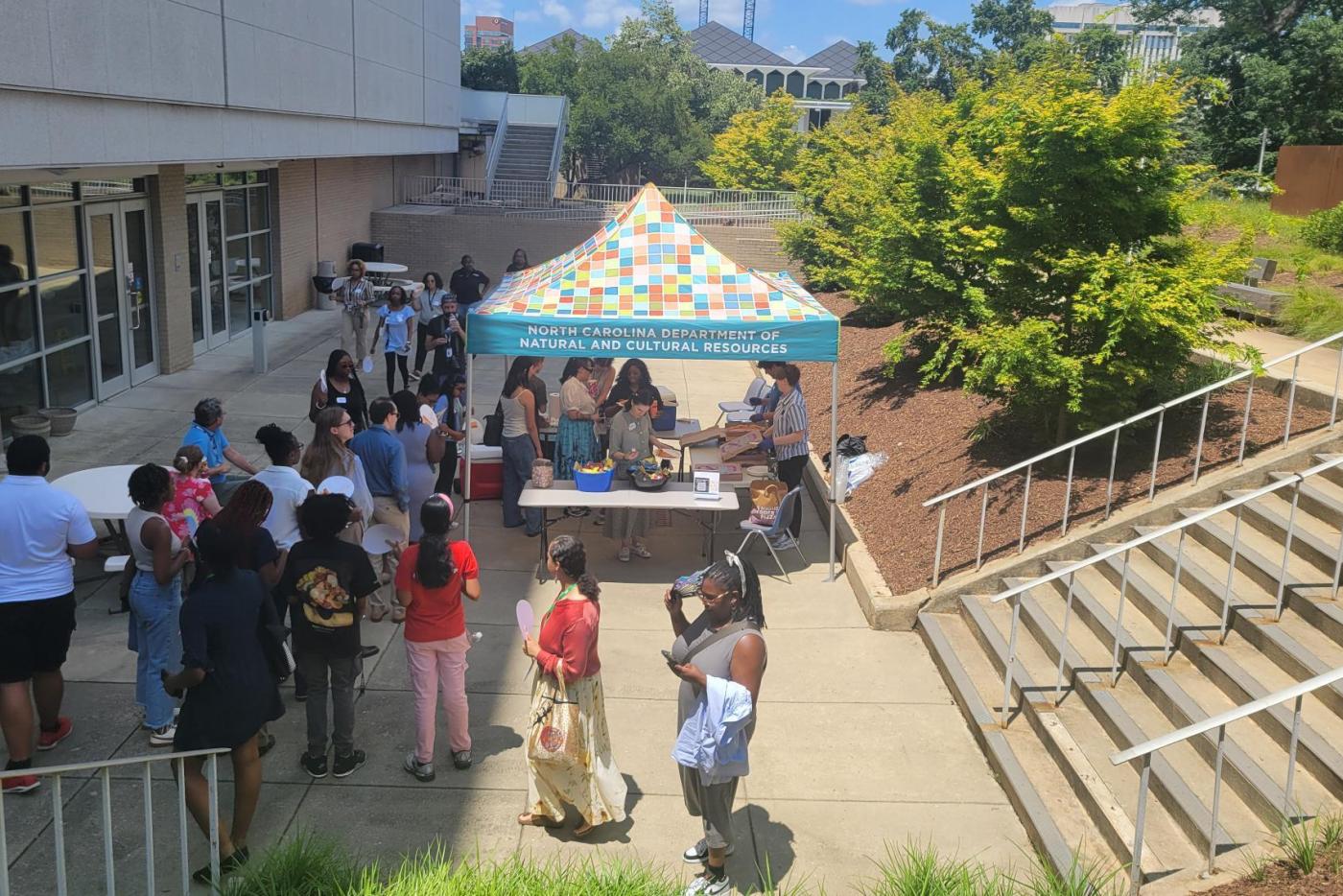 Crowd of people standing outside on pavement around a tent at an event