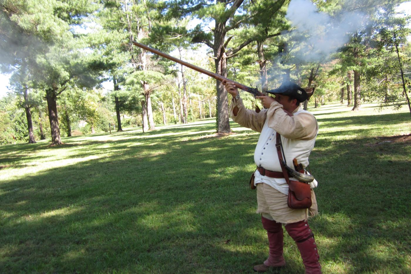 A historical interpreter dressed as a Revolutionary era soldier firing a musket.