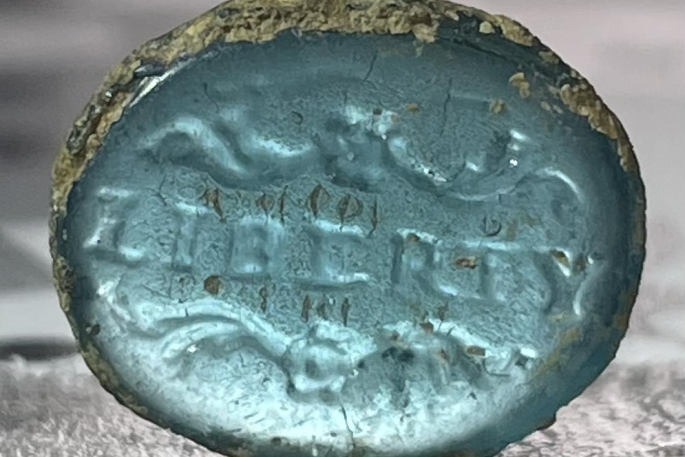 close up image of a teal cuff link with the word "liberty" stamped onto it 