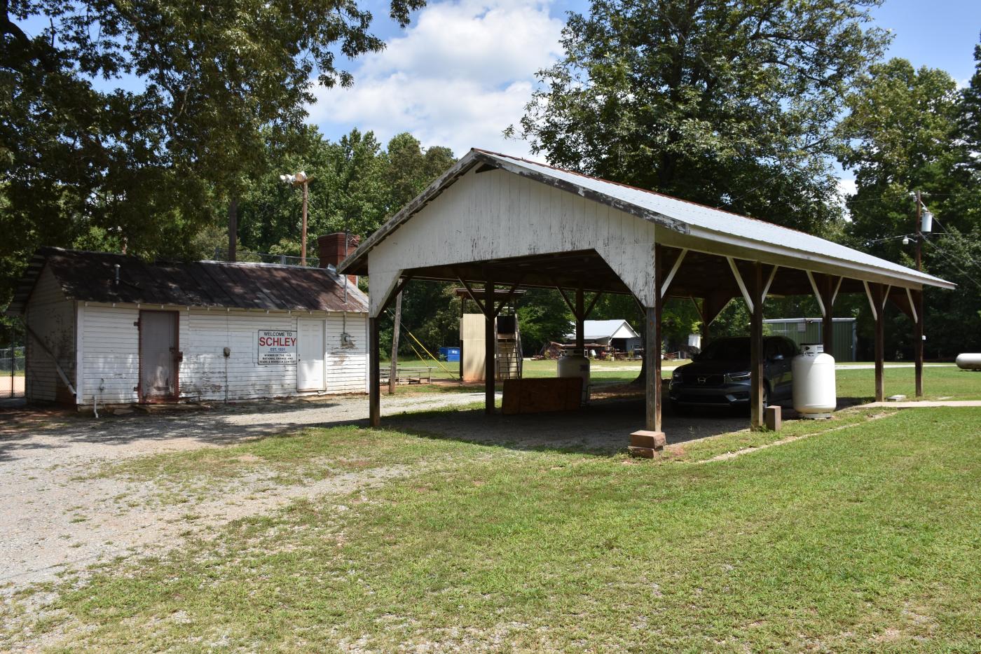 Outdoor shed and canopy on green grass, trees and blue sky in the background