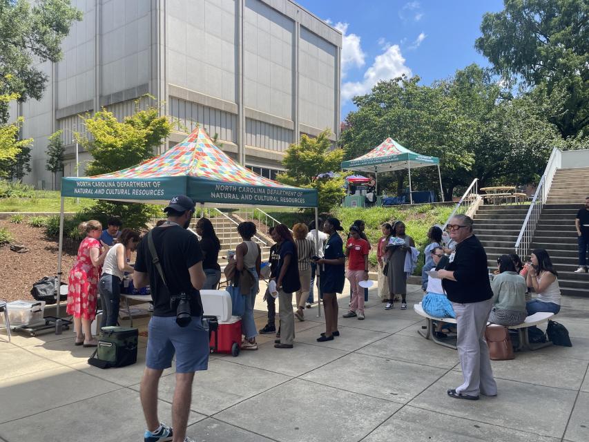 Crowd of people standing outside on pavement around a tent at an event
