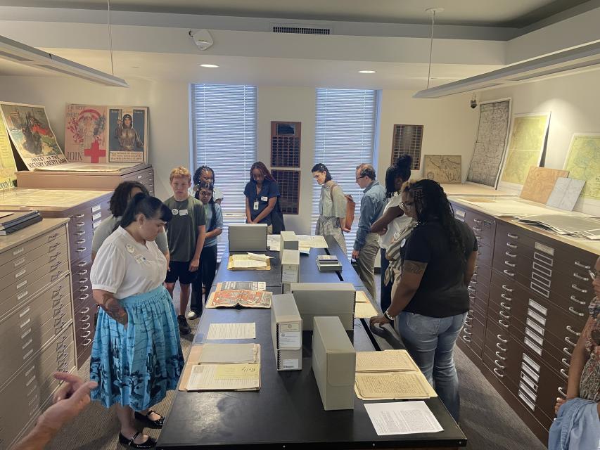 group of people standing in a line around a table of old documents