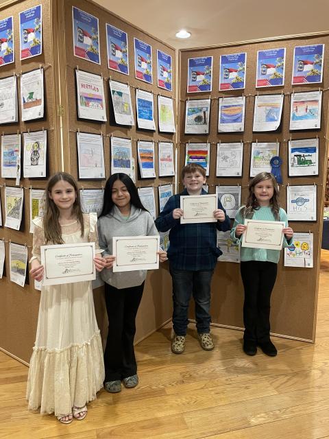 Children hold certificates in front of a wall of art