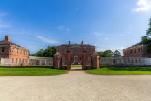 Three brick colonial buildings at Tryon Palace with a fence and ornate brick entrance in front of them.