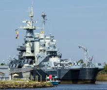 A grey battleship docked on a river with colorful signal flags on the ship.