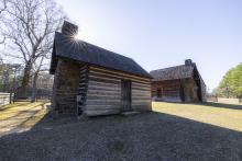 Two log cabins with stone chimneys sit on a grassy lawn.
