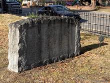 Memorial Stone on grass, with a street in the background