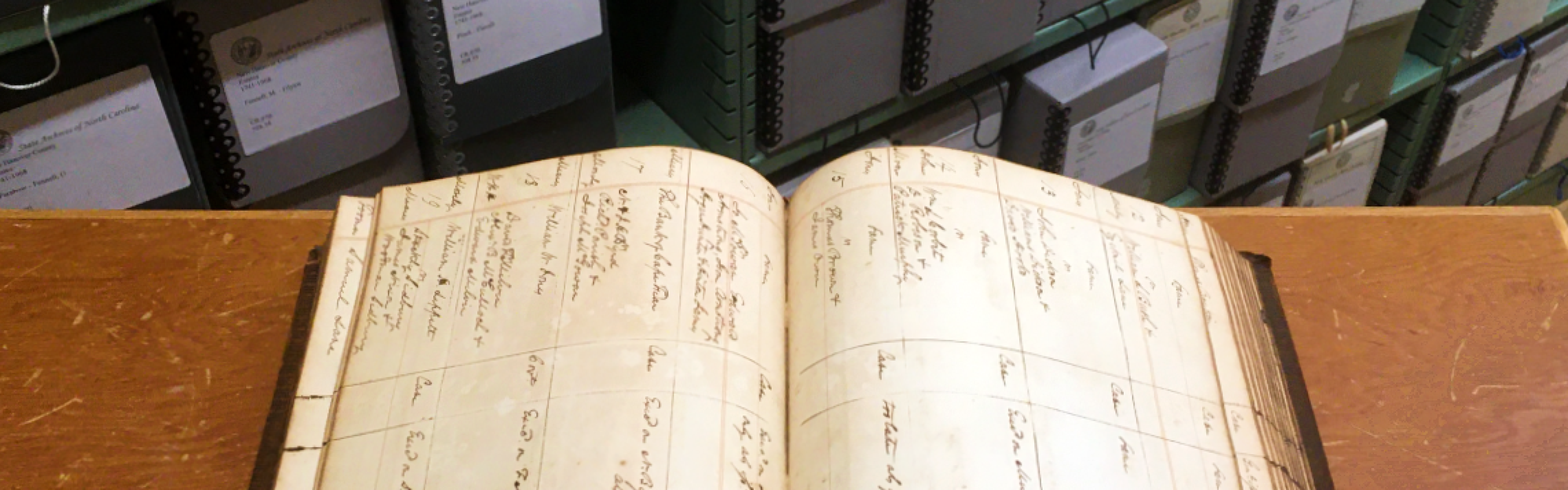 Open book on a table in front of stacks of archival fibredex boxes. 