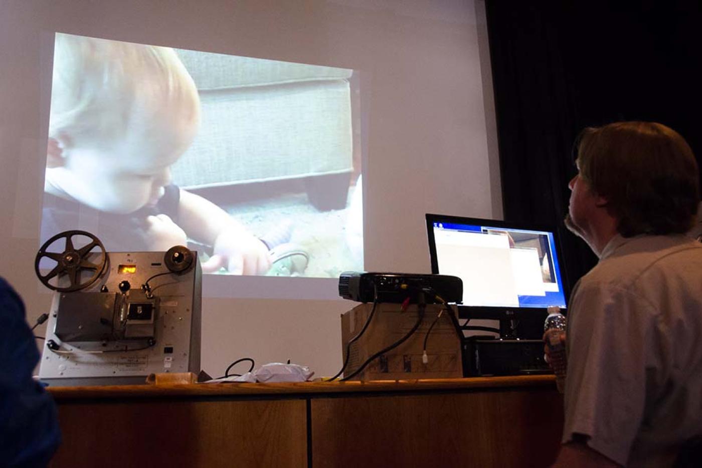 Researcher digitizing a home page from film to digital format in front of a laptop and projector screen. 