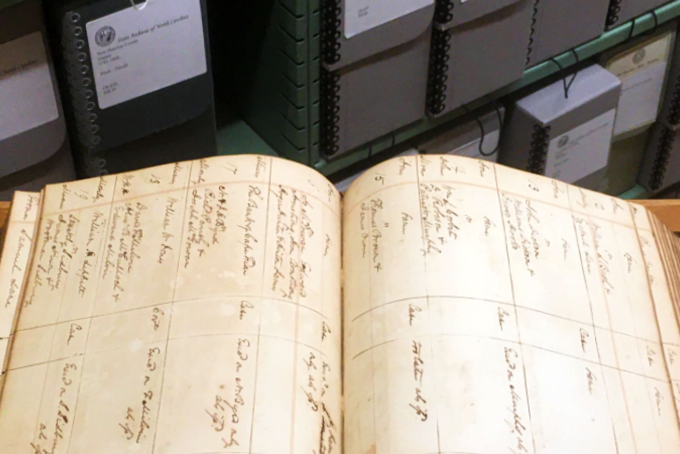 Open book on a table in front of stacks of archival fibredex boxes. 