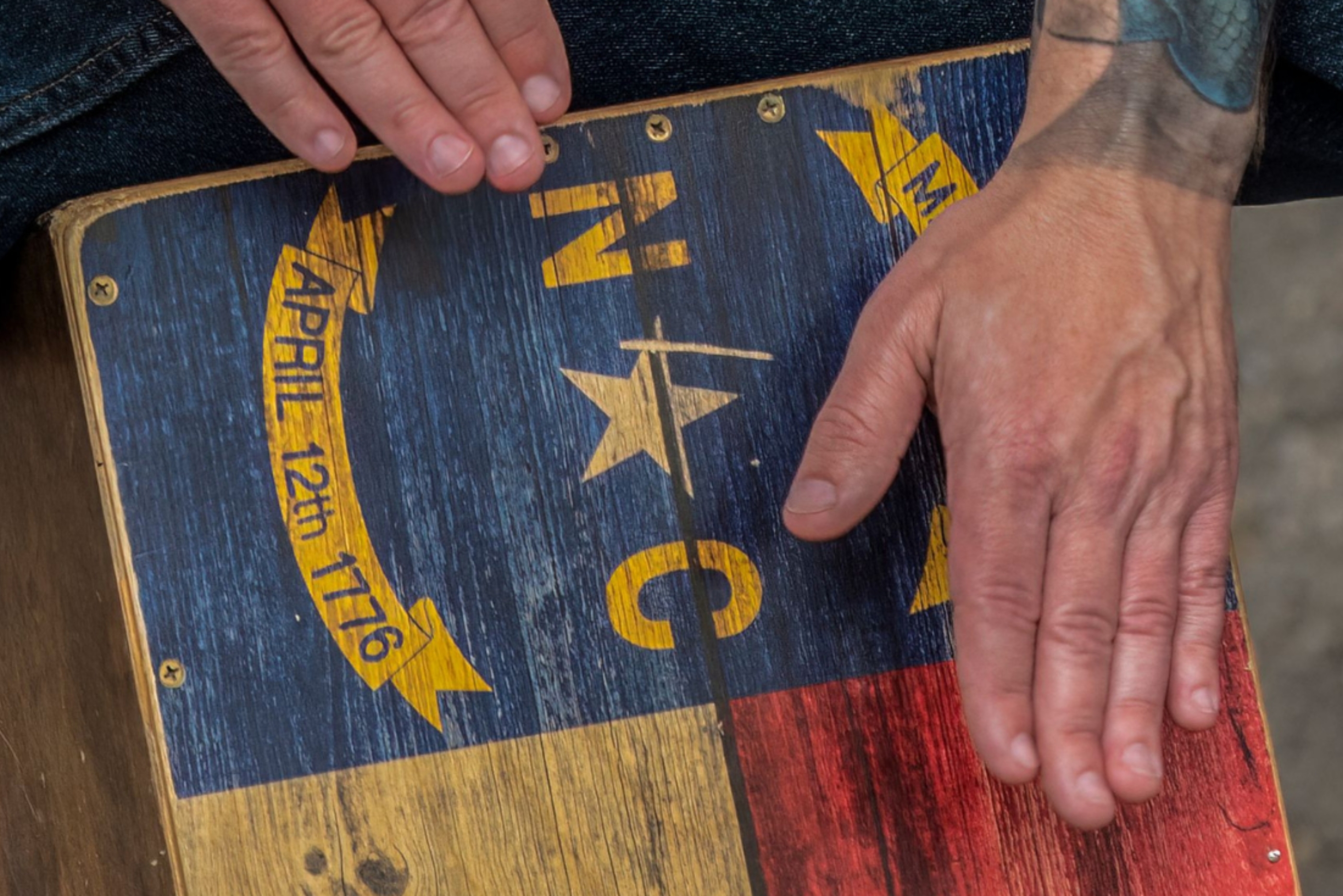 hands playing a box drum painted with the NC state flag