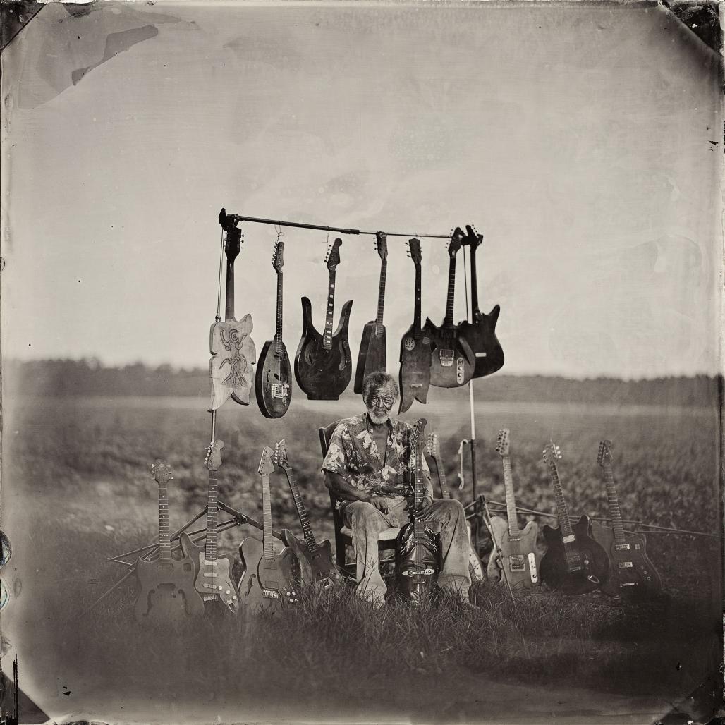 Musician and guitar maker Freeman Vines sitting in a field surrounded by guitars he has made