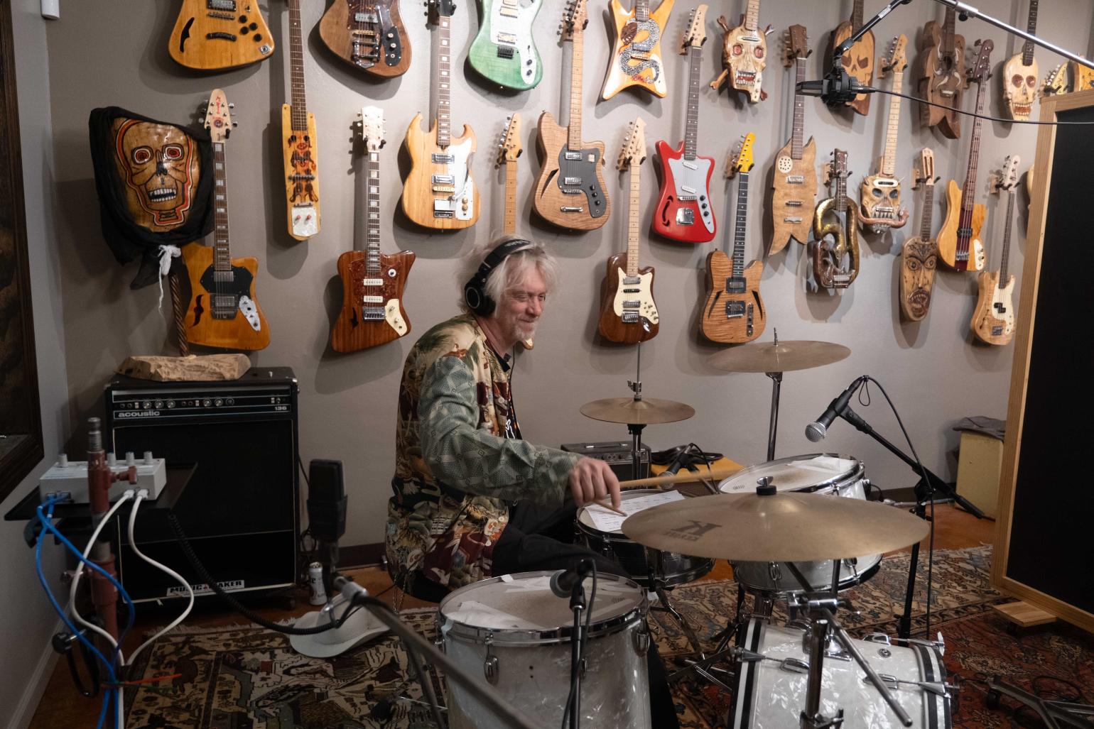 Musician Jimbo Malthus playing the drums at the Music Maker Studio, sitting in front of a wall full of guitars