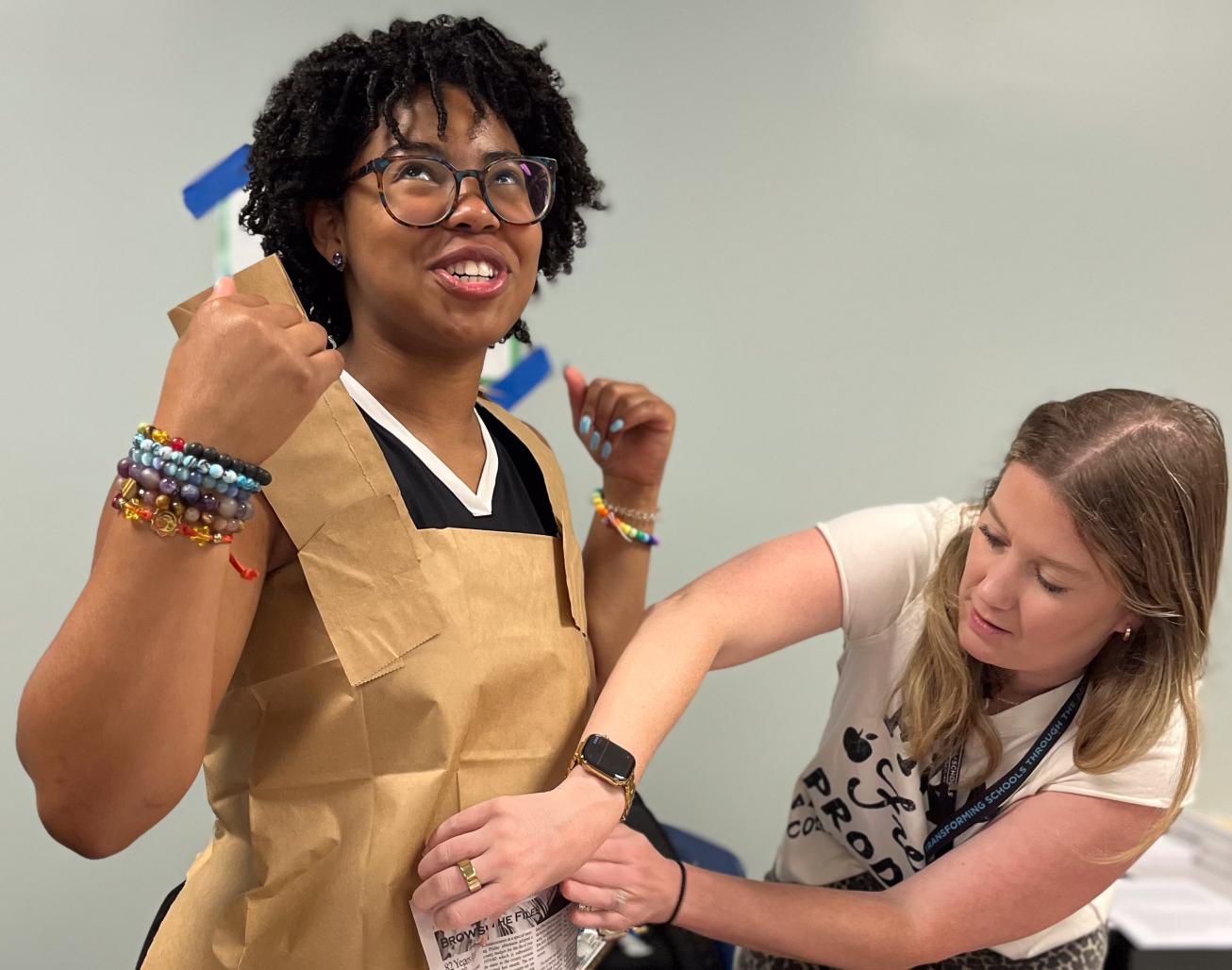 A woman taping a paper dress on another woman