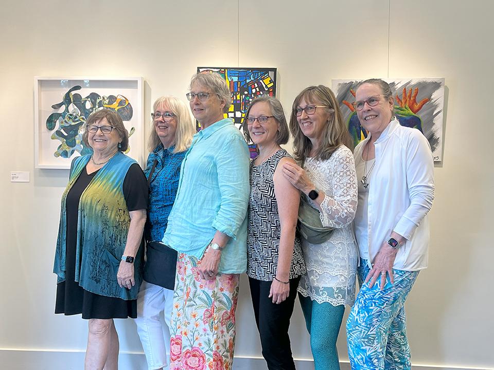 Six women pose in front of artwork.