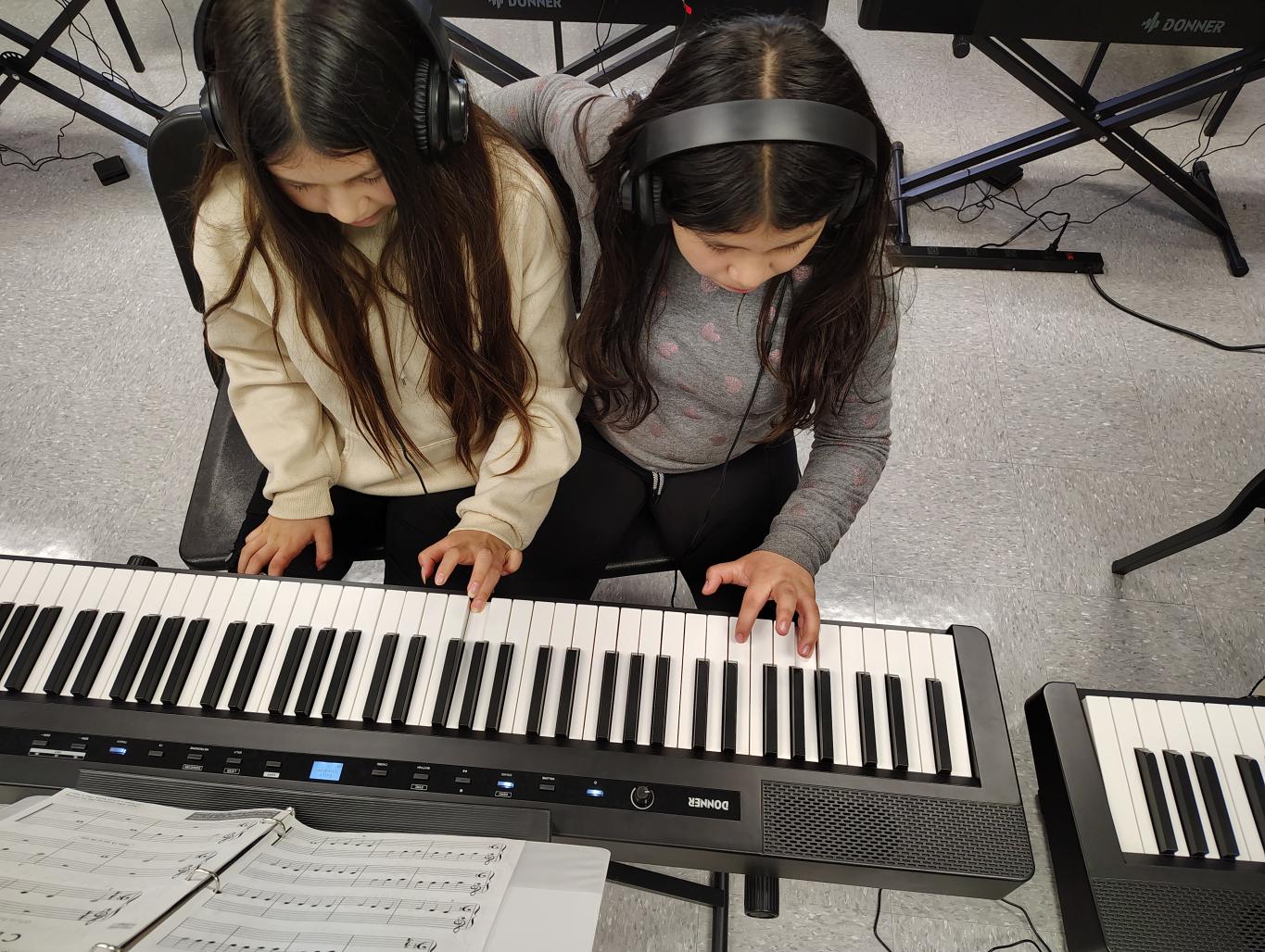 two piano pupils share a duet at the keyboard