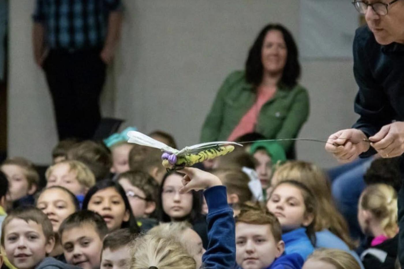 Hobey Ford performing for a student audience with a dragon fly puppet. Photo courtesy of Hobey Ford and Loyd Artists
