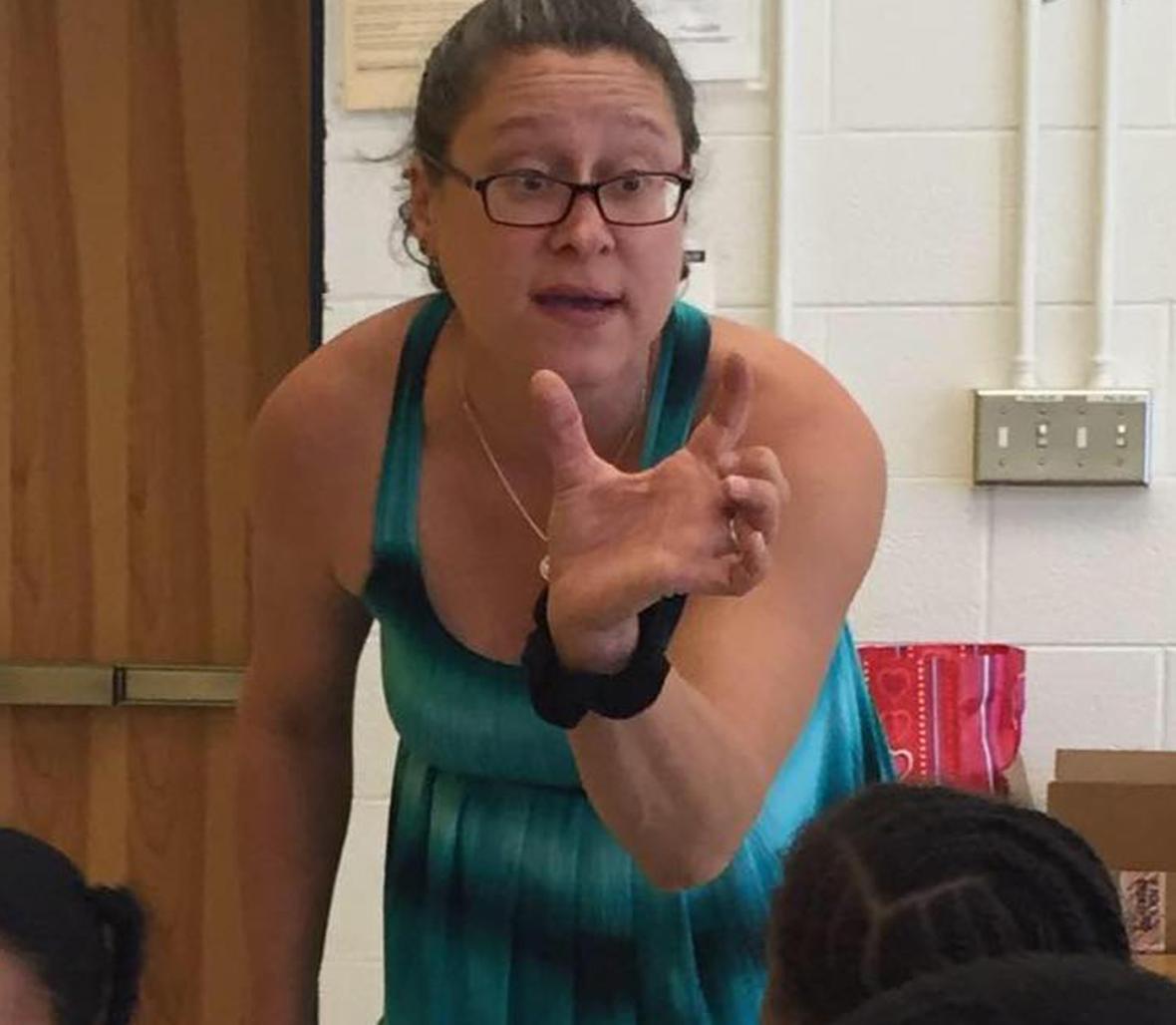 A woman leaning over a desk and gesturing with her hands.