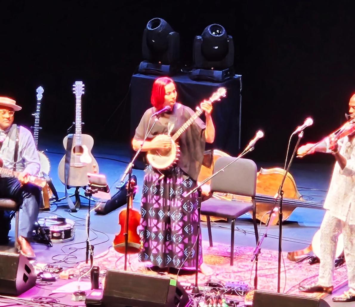 three musicians on stage, playing a guitar, banjo, and violin