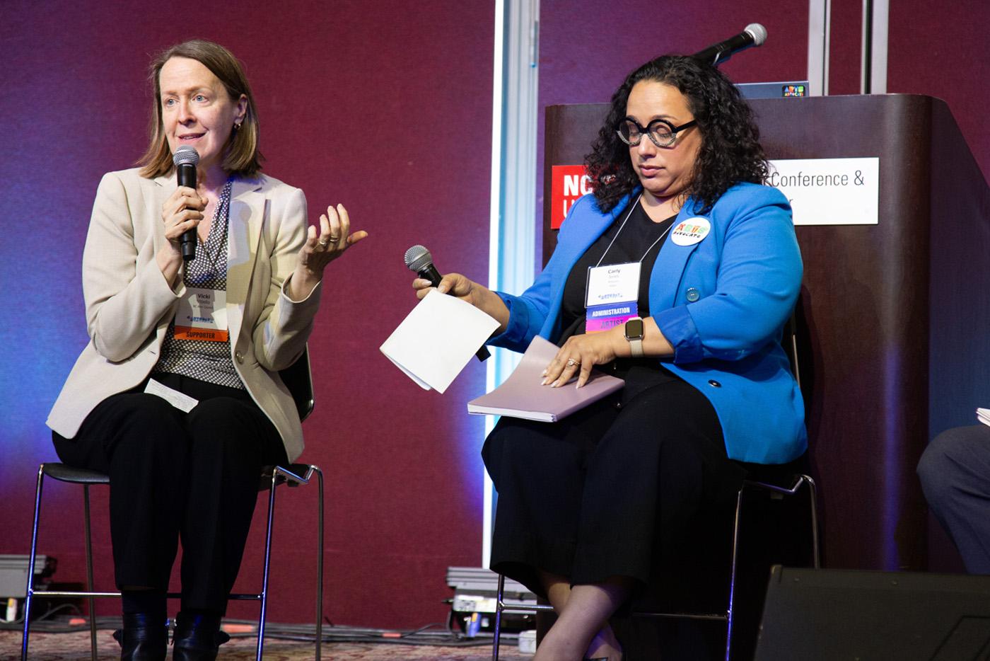 Two women seated and speaking with microphones. 