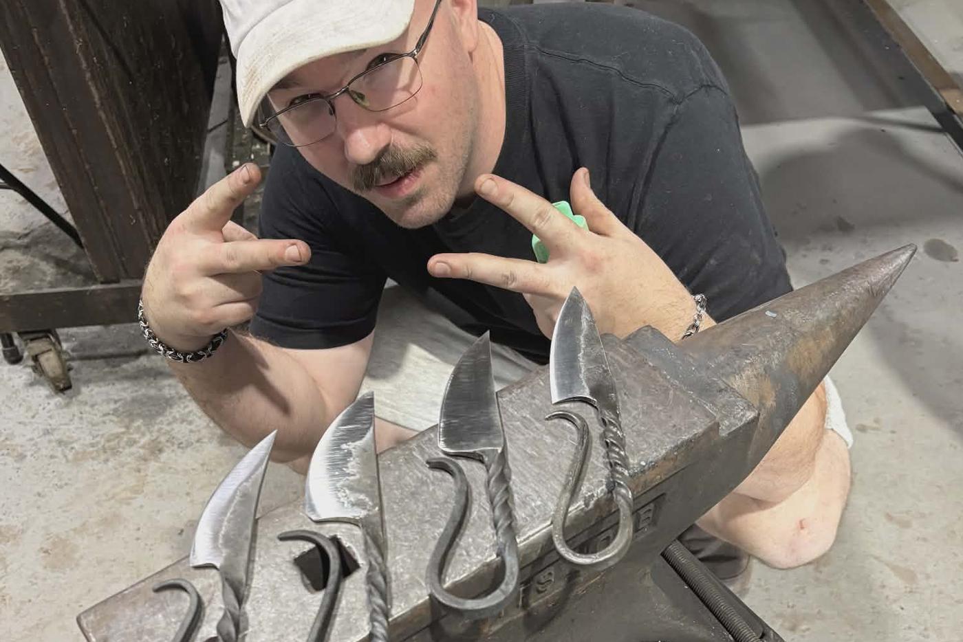 Artist poses with set of hand-crafted knives on an anvil.