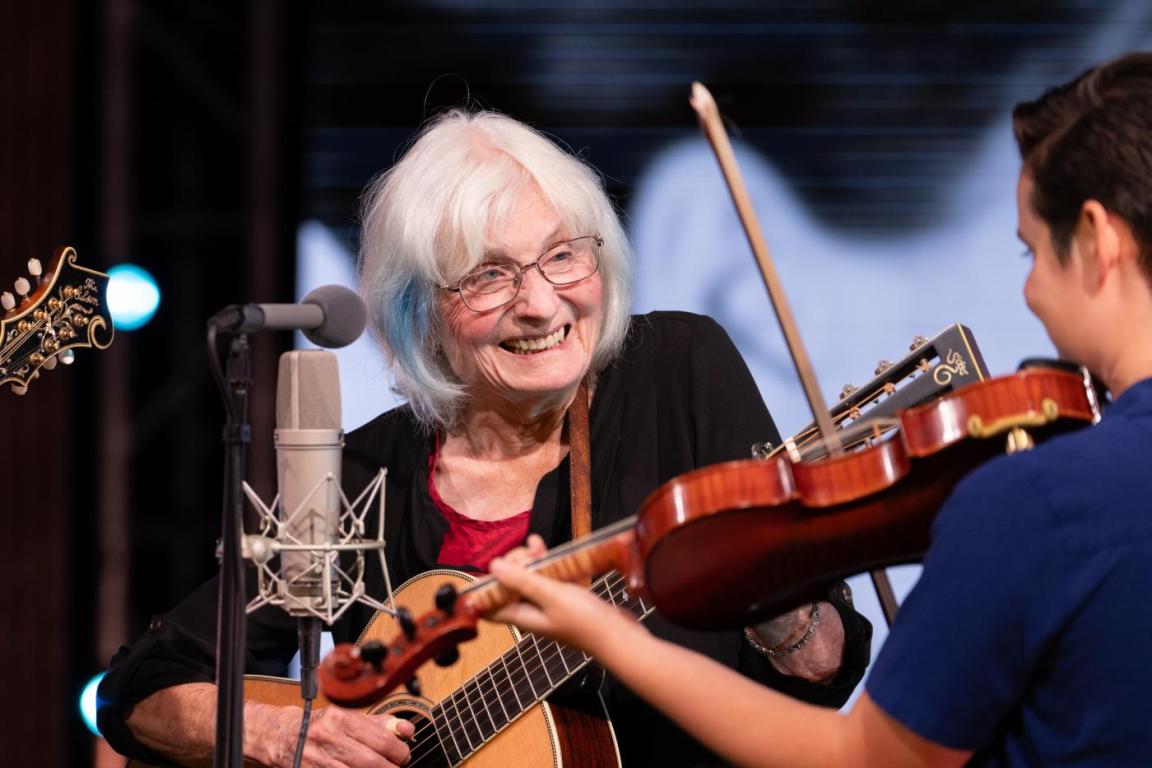 Alice Gerard plays guitar on the Shaped by Sound stage and smiles at fiddler Tatiana Hargreaves