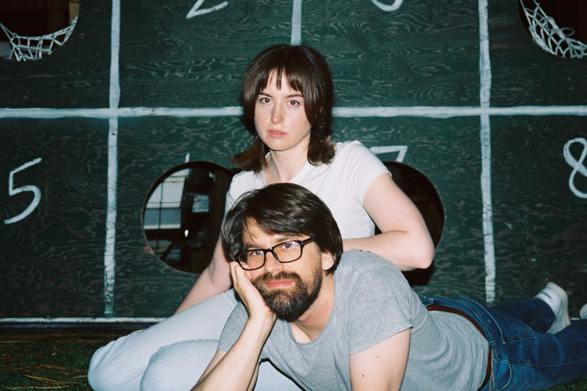 two-piece Gibson & Toutant pose in front of a green and white sign