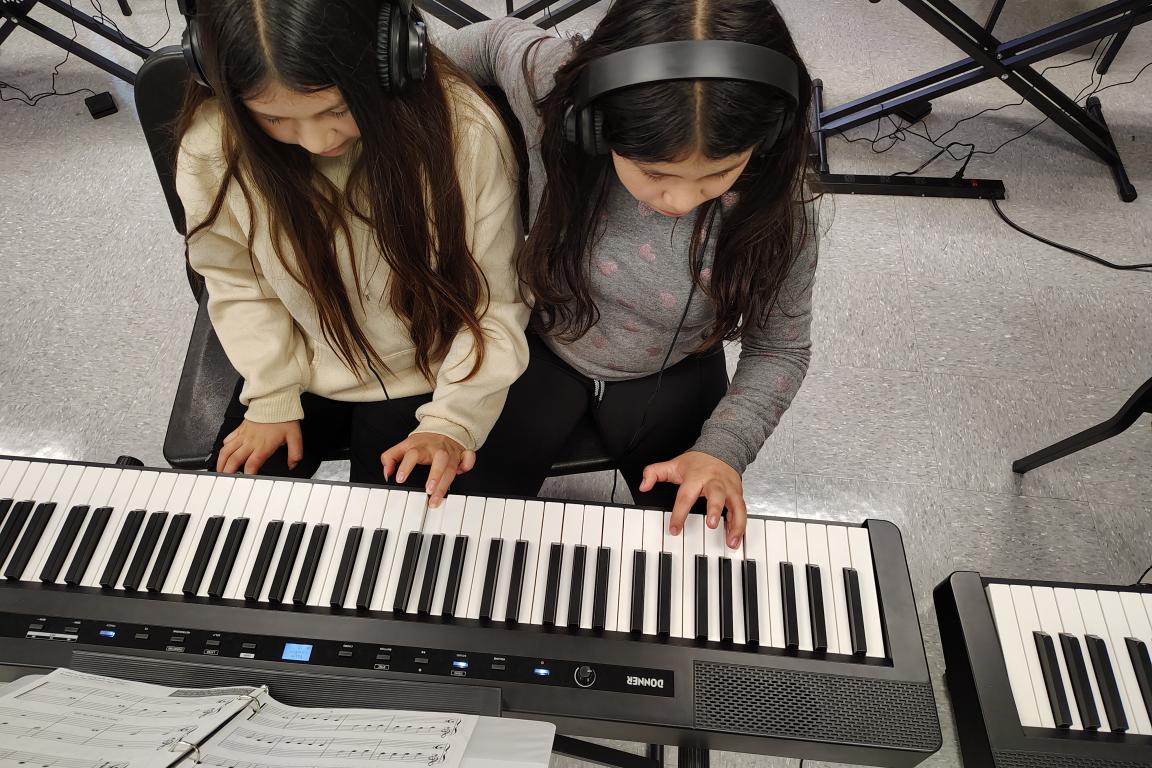 two piano pupils share a duet at the keyboard