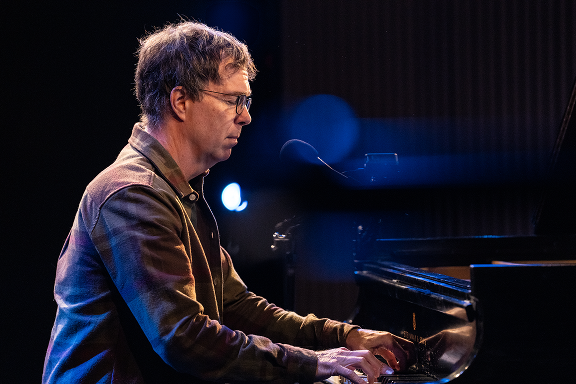 Ben Folds profile view at piano in dark light