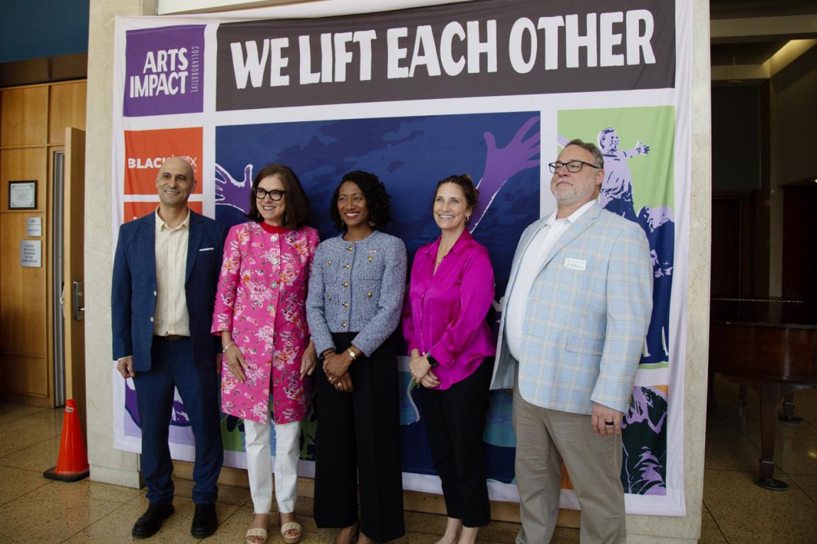 Five people stand in front of a banner that says Arts Impact, We Lift Each Other